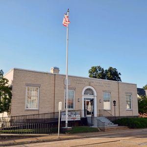 Single-story brick building with arched doorway window and flag pole on street