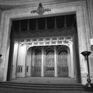 Interior of room with stage with arched stained glass windows behind it