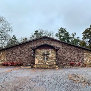 Brick and stone church building with bell on parking lot