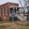 Brick building with covered porch stairs and historic marker sign