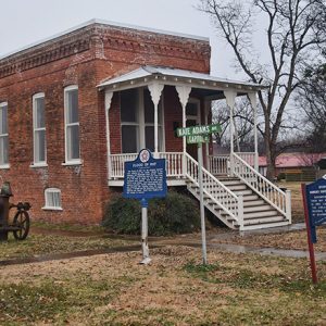 Brick building with covered porch stairs and historic marker sign