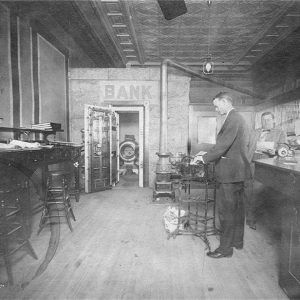 Two white men in suits working inside bank with open vault in the background