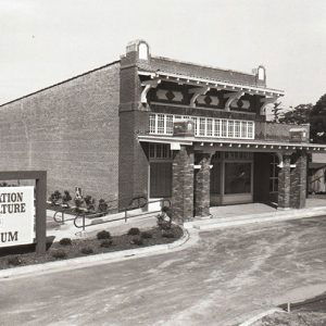 Two-story brick building with covered porch next to parking lot and sign "Plantation Agriculture Museum"