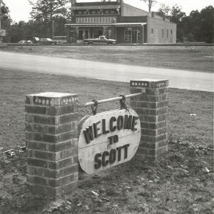 Multistory brick building with "Welcome to Scott" sign in the foreground