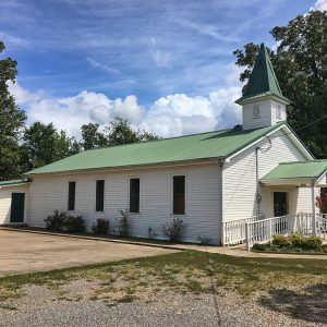 Green and white church building with steeple and side parking lot