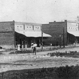 Brick storefronts and people walking on dirt road