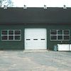 Green building with central garage bay door and truck parked outside