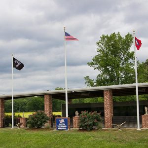 Memorial wall under pavilion with brick columns and three flag poles outside it