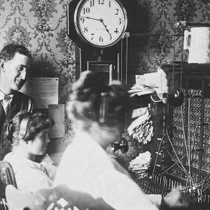 White man with glasses in suit with white female switchboard operators at work