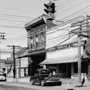 Town street with brick buildings cars and telephone lines entering second story window of two-story building