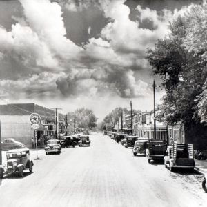 Street lined with buildings and parked cars beneath cloudy skies