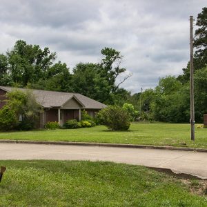 Single-story building with covered entrance next to parking lot with sign on grass