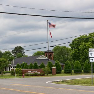 Brick building with Dutch gable roof and tower inside fence with brick sign on street corner