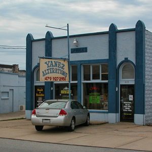 Silver car parked outside single-story buildings with hanging sign saying "Yanez Alterations"