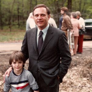 White man in suit and tie with white boy in striped shirt