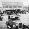 Cars parked outside brick storefronts on dirt road