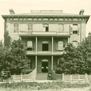 Front view of multistory building with covered porch and balcony inside wooden fence