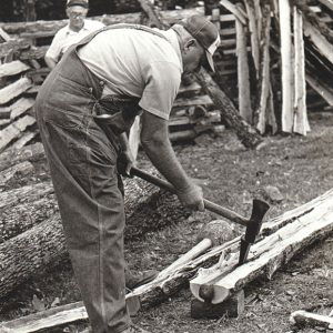 White man in overalls splitting rails while another white man watches