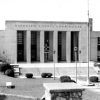 Multistory stone brick building with carved "Randolph County Courthouse" art deco columns and large courtyard with round bushes