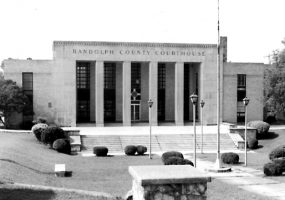 Multistory stone brick building with carved "Randolph County Courthouse" art deco columns and large courtyard with round bushes