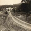 Looking down dirt road on hill with multistory buildings in the background and trees on the right