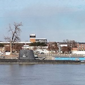 Submarine in river with dock and city buildings in the background