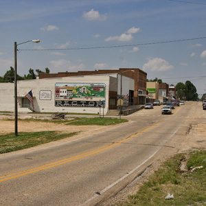 Traffic driving by brick storefronts on two-lane town road