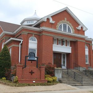 Multistory brick building with dome and bell on brick pedestal