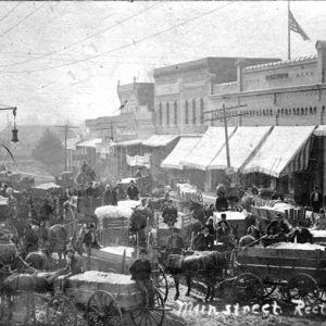 Horse drawn wagons loaded with cotton and white drivers in crowded town street