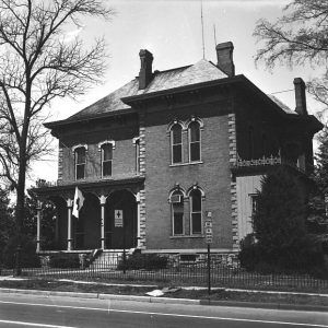 Multistory brick house with covered corner porch inside iron fence