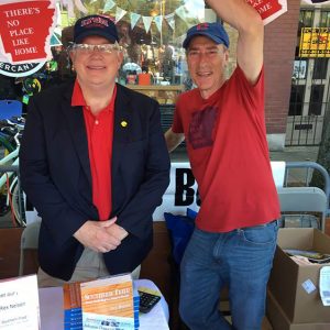 Two white men smiling with books on table in front of them