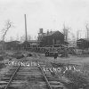 Railroad tracks with industrial buildings and water tower signed "cotton gins Reyno Ark"