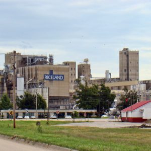 Multistory brick and steel industrial building complex with "Riceland" logo visible on center building