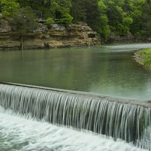 River and spillway with tree covered rock walls and shore