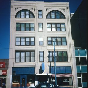 Five-story hotel building with arched windows on top floor and striped awing on first floor over the words "hotel restaurant" painted on front window