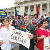 Crowd of men and women with flags and protest signs on steps of state capitol building