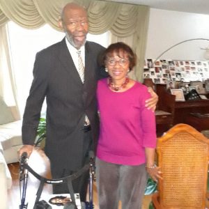 Older African-American man in suit posing with African-American woman with glasses in pink top