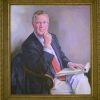 White man in suit and glasses sitting with notepads