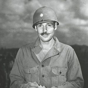 white man with mustache in military uniform with helmet holding a pack of cigarettes