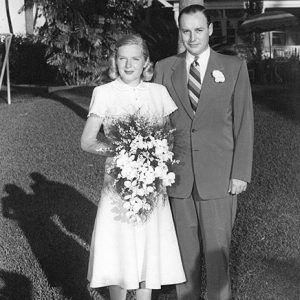 white blond woman in dress holding flowers standing next to white man in suit and tie