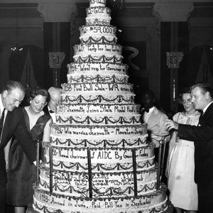 Mixed crowd admiring multitiered cake with text on it