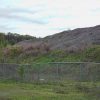 Grass covered mound with "Rocky Point Minerals" sign on it inside fence