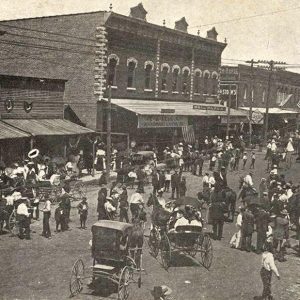 Horse drawn carriages and people on crowded town street