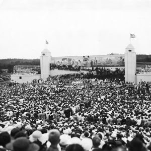 large crowd fills stadium, platform decorated with banners in the distance