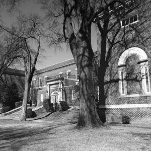 Two-story brick school building with balcony and trees