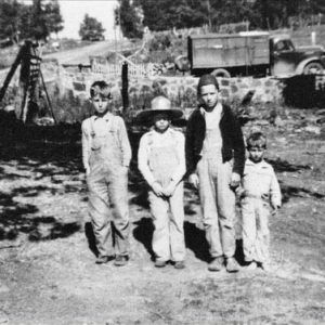 Four white boys standing with truck and stone wall behind them