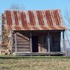 Abandoned log cabin with rusted metal roof and covered porch and stone chimney