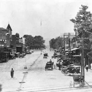 Cars and wagons on town street with two-story brick buildings