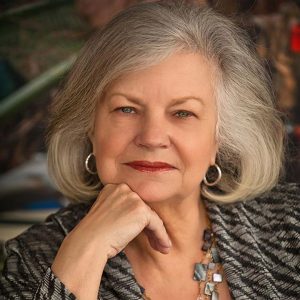 Older white woman with long gray hair in striped shirt and earrings