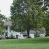 Multistory house with covered porch and gazebo on grass with trees in its front yard